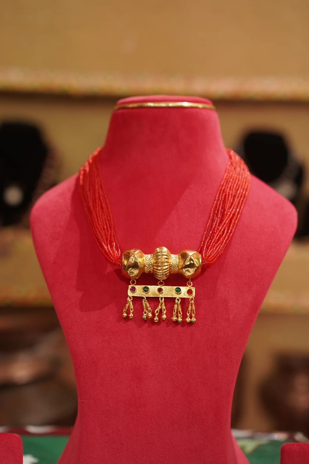 Contemporary Timaniya necklace with red strands, three gold-coloured central elements and small hanging details.