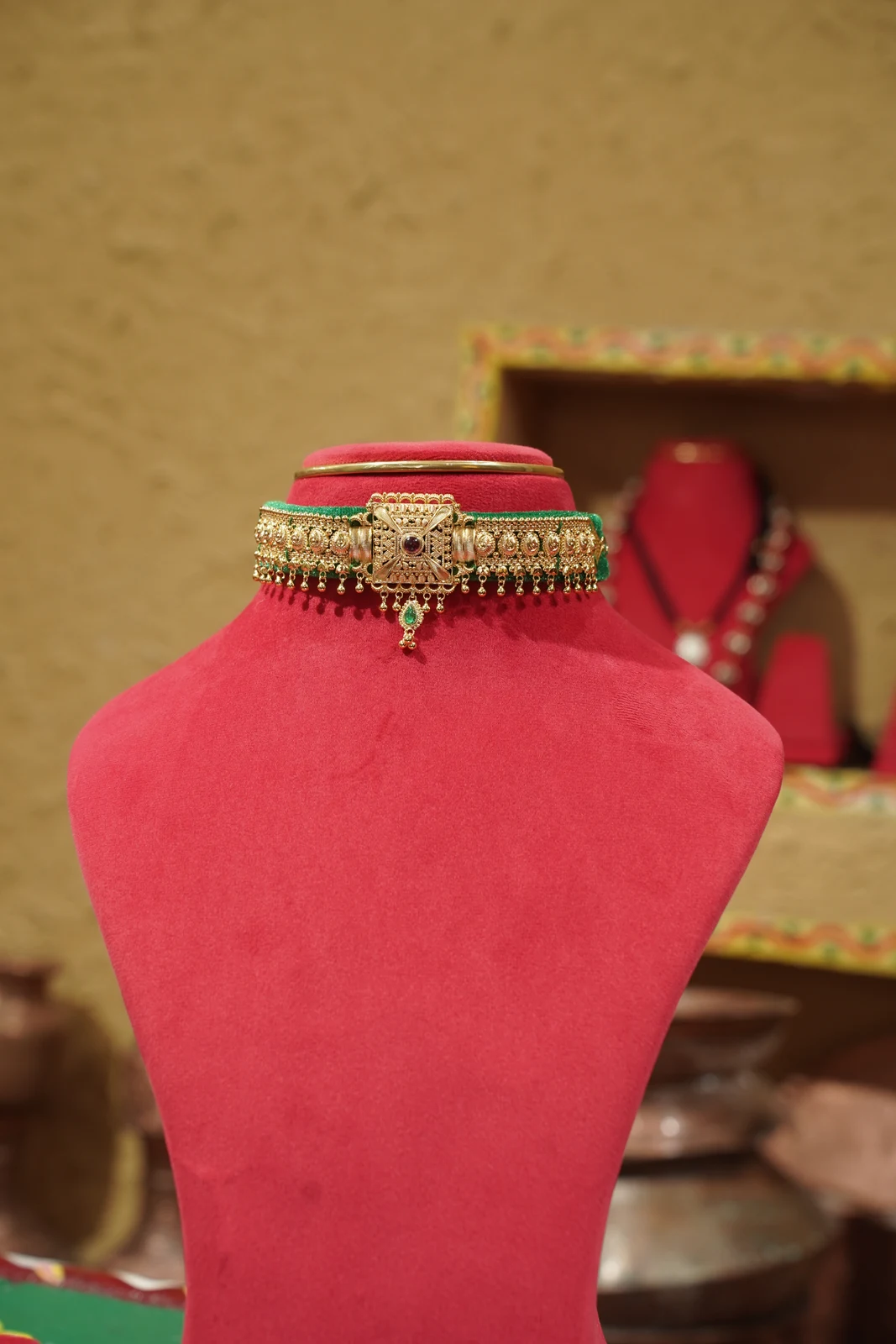 Contemporary gold-coloured Guloband with green edging and a central decorative panel, shown on a red display bust.