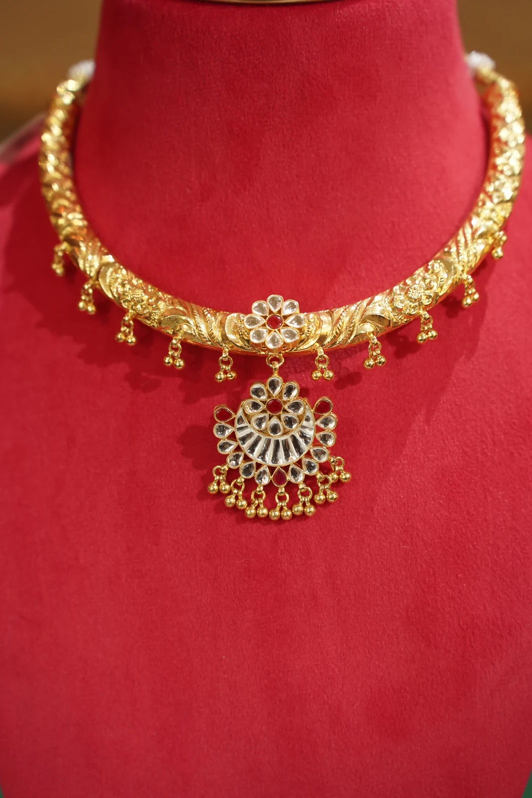 Close view of the floral pendant and hanging details on a contemporary gold-coloured Hansuli collar.
