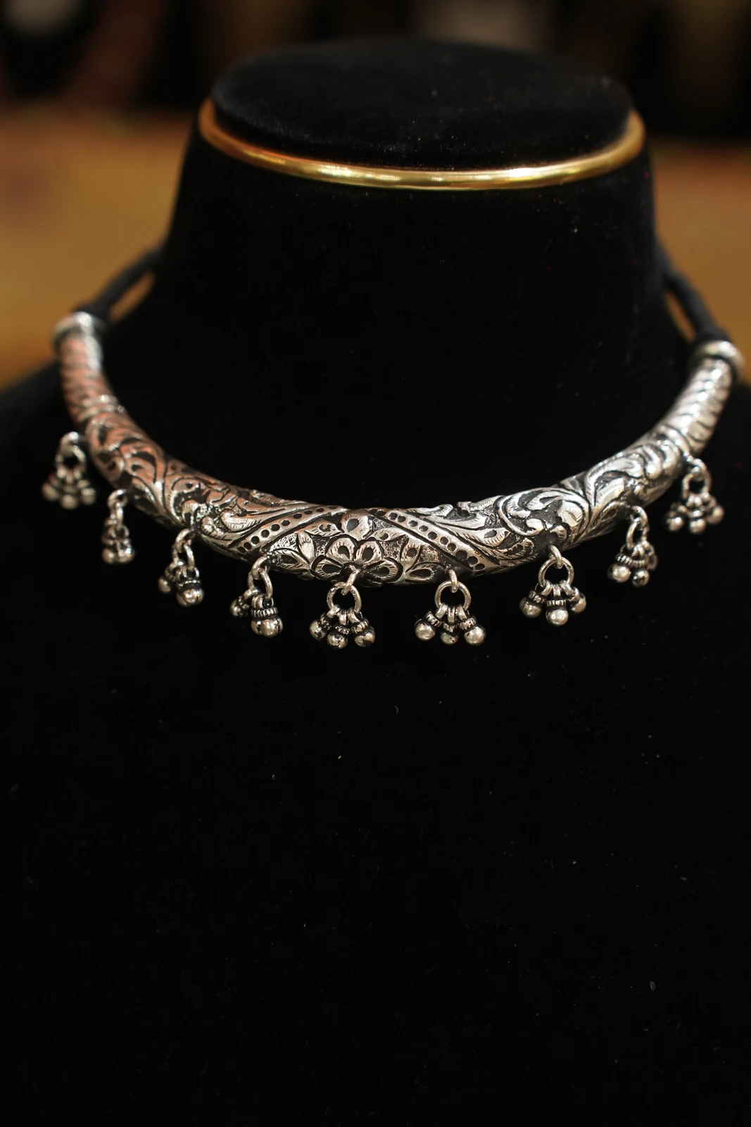 Close view of the scrolling surface pattern and hanging clusters on a contemporary silver-coloured Hansuli collar.